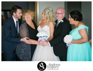 bride, mum, dad and siblings looking at brother laughing during family photo