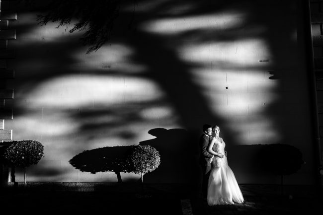 bride and groom outside Eschol Park House standing against wall, sun shines through leaves and makes dramatic shadows on the wall.